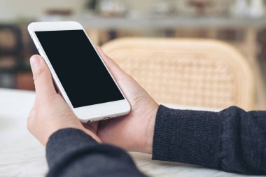 Modern cafe 'de boş siyah masaüstü ekranlı beyaz cep telefonu tutan ellerin görüntüsü