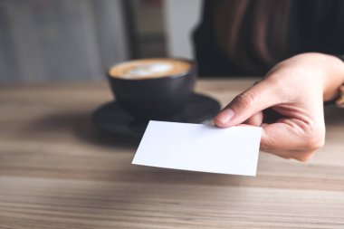 İş kadını ofisinde kahve fincanı olan birine boş bir kartvizit veriyor.