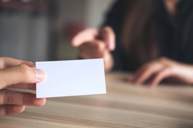 Arka planda iş kadını olan boş bir kartvizit tutan bir işadamı.