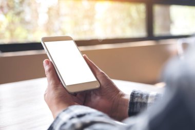 Kafede boş masaüstü ekranı olan beyaz cep telefonu tutan ellerin görüntüsü