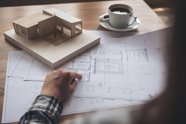 Mimari bir model üzerinde çalışan bir mimar. Masaya kağıt ve kahve fincanı çiziyor.