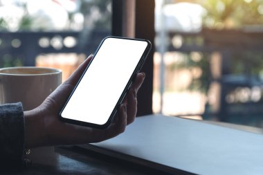 Kafedeki masada kahve fincanı ve dizüstü bilgisayarı olan, boş beyaz ekranlı, siyah cep telefonlu bir kadının el resmi.