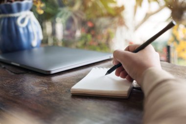 Ahşap masanın üzerine boş bir deftere el yazısının yakın plan resmi. 