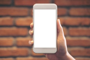 El ele tutuşmanın ve beyaz cep telefonunu tuğla duvar zeminli boş masaüstü ekranıyla kaldırmanın görüntüsü