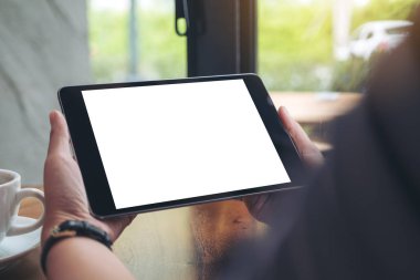 Siyah tabletli, beyaz ekran ve kafedeki ahşap masada kahve fincanı tutan bir kadının ellerini taklit et.