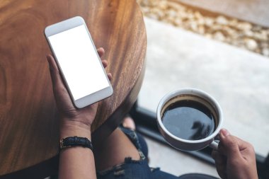 Kafede kahve içerken beyaz cep telefonlu bir kadının ellerinin boş ekran görüntüsü.