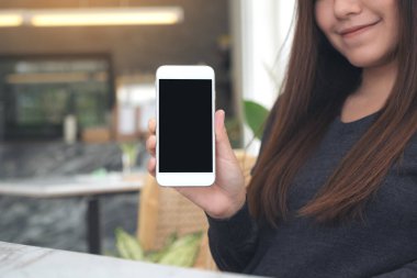 Kafedeki boş siyah ekranlı beyaz cep telefonunu tutan ve gösteren bir kadının görüntüsü.