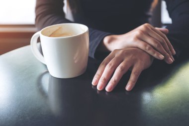 Kafede el ele tutuşup sıcak kahve içen bir kadının yakın plan görüntüsü.