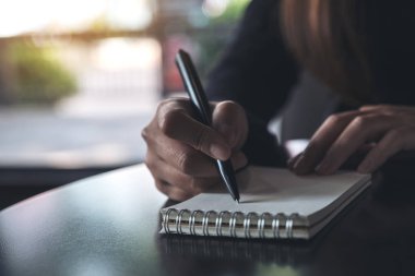 Masanın üzerine beyaz boş bir defter yazan bir kadının ellerinin yakın plan resmi. 
