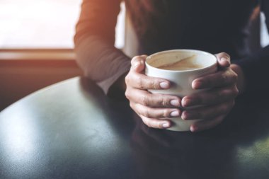 Kafede elinde sıcak kahve tutan ve içen bir kadının yakın plan görüntüsü.