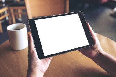 Siyah tabletli, beyaz ekranlı ve kafedeki kahve fincanının olduğu ellerin görüntüsü. 