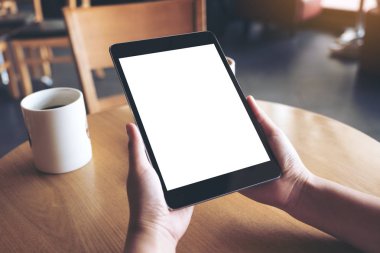 Siyah tabletli, beyaz ekranlı ve kafedeki kahve fincanının olduğu ellerin görüntüsü. 