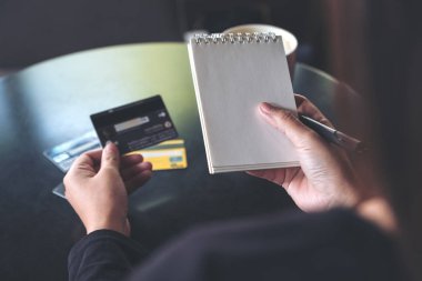 Masada elinde beyaz bir defter ve kredi kartı olan bir kadının yakın plan fotoğrafı. 