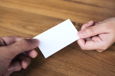 İşadamı, ahşap masa arkasındaki iş kadınına boş bir kartvizit veriyor.