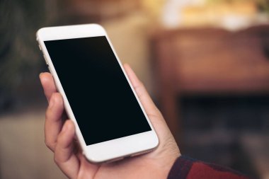 Kafedeki boş siyah ekranlı beyaz cep telefonlu el görüntüsü.