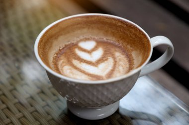 Masanın üzerinde kalp lattesi olan bir fincan sıcak kahvenin yakın plan resmi.