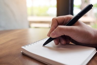 Masanın üzerine beyaz boş bir defter yazan bir kadının ellerinin yakın plan resmi. 