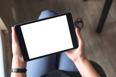 Ofiste boş beyaz masaüstü ekranlı siyah tablet bilgisayarı tutan ve bacak bacak üstüne atmış bir kadının en üst görünüm görüntüsü