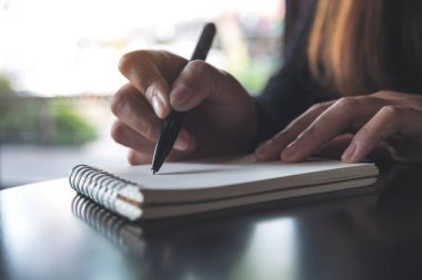 Masanın üzerine beyaz boş bir defter yazan bir kadının ellerinin yakın plan resmi. 