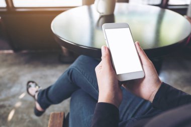 Kafedeki boş masaüstü ekranlı beyaz cep telefonu tutan bir kadının el resmi.