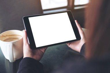 Siyah tabletli, beyaz ekranlı ve kafedeki kahve fincanının olduğu ellerin görüntüsü. 