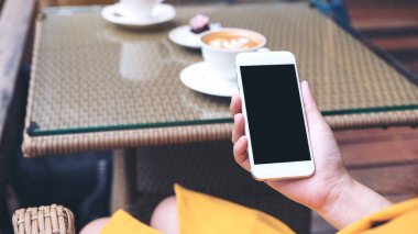 Kafedeki boş siyah ekranlı beyaz cep telefonlu bir kadının el resmi. 