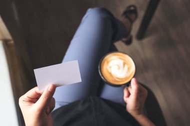Kahve fincanı içerken elinde boş bir kartvizit tutan bir kadının en iyi görüntüsü.