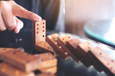 Tahta domino oyununun masaya düşmesini engellemeye çalışan bir elin yakın plan görüntüsü.