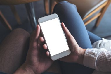 Kadın ve erkeğin el ele tutuşup boş masaüstü ekranlı beyaz cep telefonuna bakarken görüntüsü. 