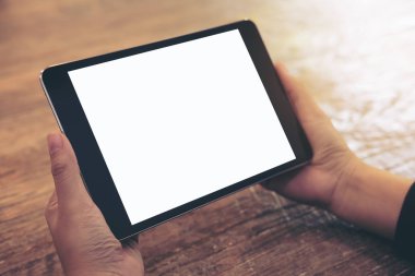 Cafe ahşap masa arka plan üzerinde siyah tablet pc ile beyaz boş perde holding eller mockup görüntü
