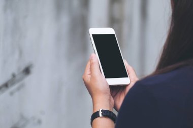 Bir kadın tutarak ve açık ve eski beyaz beton duvar arka planda boş siyah perde ile beyaz akıllı telefon kullanarak mockup görüntü