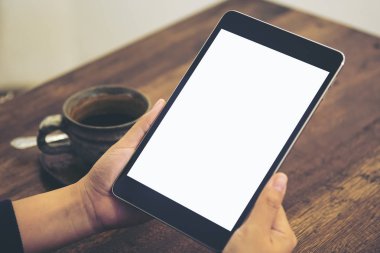 Boş beyaz ekran ve kahve fincanı ahşap masa arka plan üzerinde siyah tablet pc kafede holding eller mockup görüntü