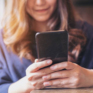 Kullanarak ve modern loft kafede siyah bir akıllı telefon bakarak gülen yüz ile güzel bir Asyalı kadın