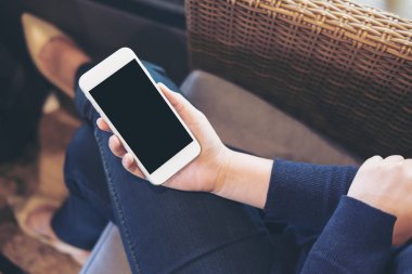 Bir kanepede oturan uylukta boş siyah perde ile beyaz cep telefonu tutan bir kadın eli mockup görüntü