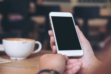 Beyaz cep telefonu ile boş siyah perde ile kahve fincanı ahşap tablo lokantada holding eller mockup görüntü