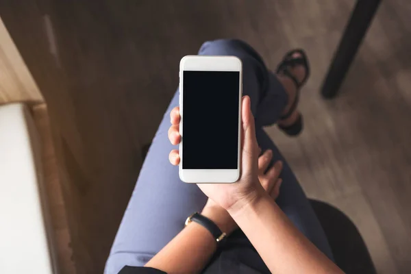 Kafede beyaz cep telefonu ve boş siyah masaüstü ekranı olan bir kadının en üstteki görüntüsü.