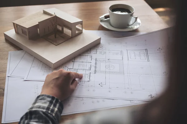 An architect working on an architecture model with shop drawing paper and coffee cup on table