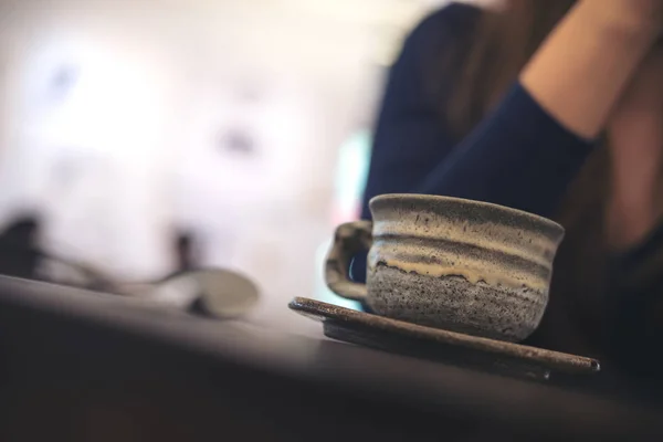 Closeup image of a woman sitting in cafe with ceramics cup of hot coffee on vintage wooden table in cafe