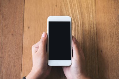 Kadının görüntüsünü mockup holding beyaz cep telefonu vintage ahşap masa arka plan üzerine boş siyah perde ile eller