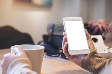 Kadının görüntüsünü mockup holding beyaz cep telefonu ile boş perde ve beyaz kahve fincanı modern loft kafede eller