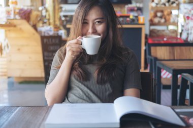 Portre resim güzel bir Asya kadının sıcak tutarak ve içme kahve modern café'iken bir kitap okuma 