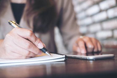 Portre resmi defter ve kullanma ve modern Cafe ahşap masa üstünde smartphone gösteren yazılı bir kadının elleri   