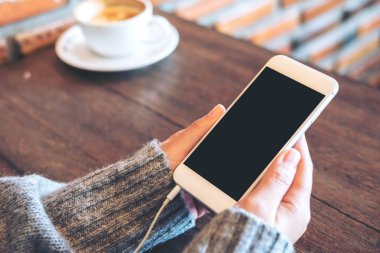 Kadının görüntüsünü mockup holding beyaz cep telefonu ile boş siyah perde ve beyaz kahve fincanı modern loft kafede eller