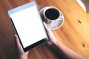 Mockup görüntü iş kadının elleri boş beyaz ekran ve ahşap masa üzerinde kahve fincanı ile siyah tablet pc kafe arka planda tutan