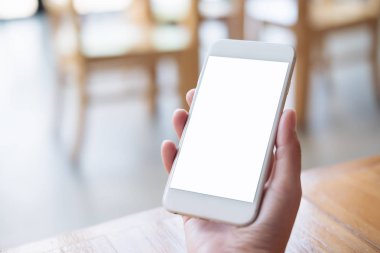 Kafede masada boş bir ekran ile beyaz cep telefonu tutan el mockup görüntü