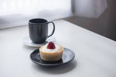 Bir çilek peynirli tart, bir fincan sıcak kahve ve kaktüs beyaz vintage ahşap masa ve perde arka planda minimalizm Cafe