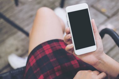 Bir kadının el vintage kafede uyluk ile ahşap zemin arka plan üzerinde beyaz cep telefonu boş siyah perde ile tutarak mockup görüntü