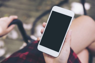 Bir kadının el vintage kafede uyluk ile ahşap zemin arka plan üzerinde beyaz cep telefonu boş siyah perde ile tutarak mockup görüntü