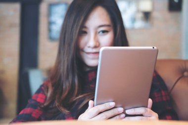 Modern kafede oturup tablet bilgisayarını kullanan ve ona bakan gülümseyen Asyalı güzel bir kadının yakın plan görüntüsü.