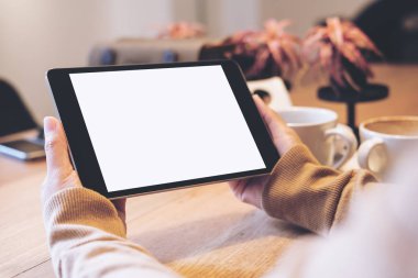 Siyah tablet pc ile kahve fincanı ahşap masa üzerinde boş beyaz ekran ile modern kafede holding eller mockup görüntü